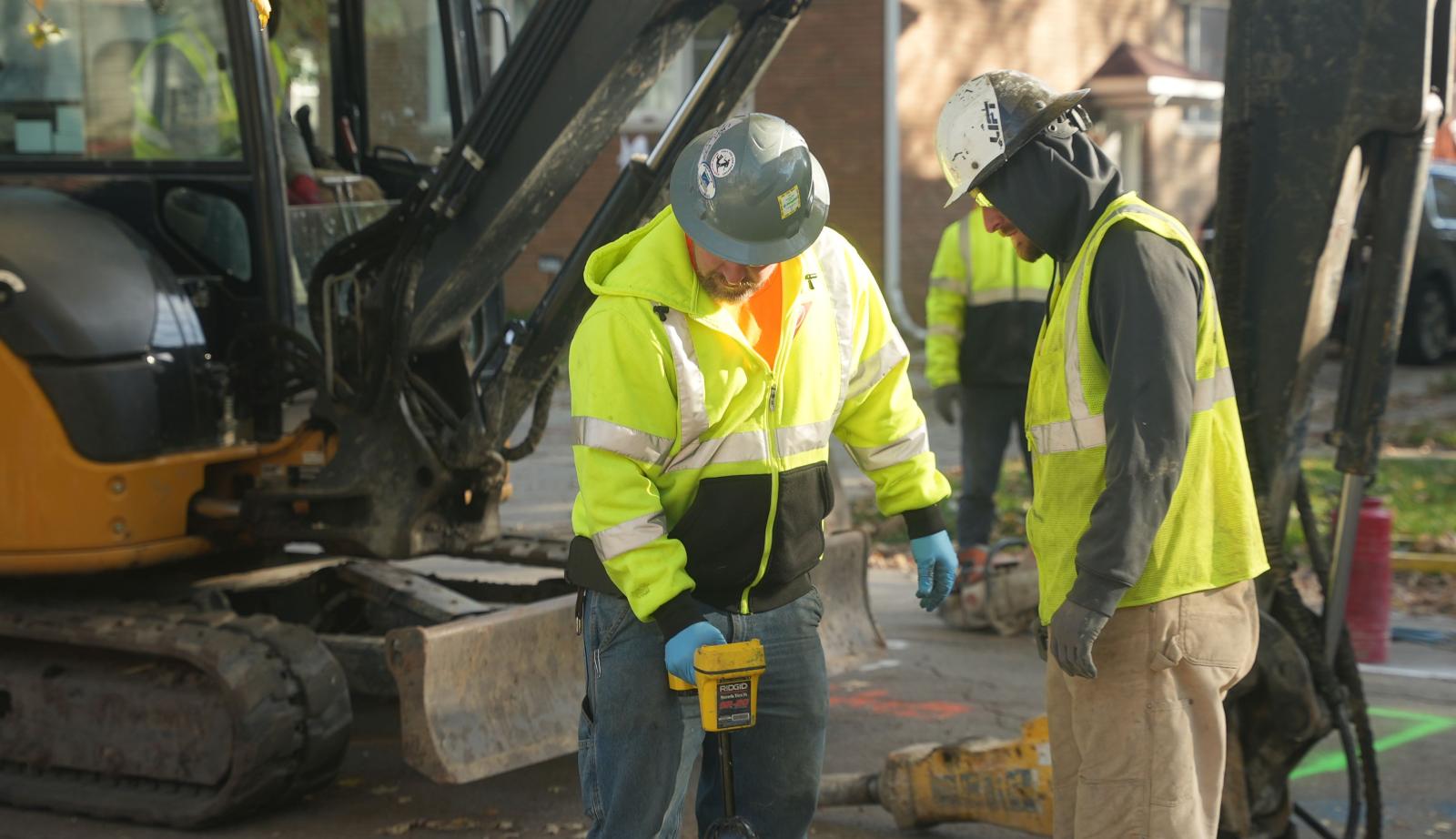 Photo of construction workers replacing a lead service pipe in the ground outside of a home.